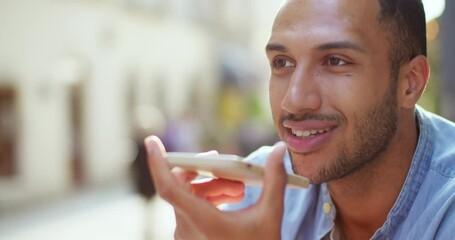 Close up of handsome young man sitting outside in city center and recording audio message on mobile phone. Male in town talking, sending voice record by smartphone. Communication via audios messages.