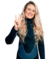 Young blonde woman wearing diver neoprene uniform showing and pointing up with fingers number three...