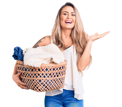 Young beautiful blonde woman holding laundry basket celebrating victory with happy smile and winner expression with raised hands - Powered by Adobe