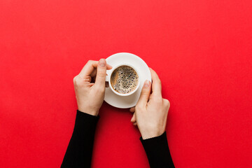 Minimalistic style woman hand holding a cup of coffee on Colored background. Flat lay, top view cappuccino cup. Empty place for text, copy space. Coffee addiction. Top view, flat lay