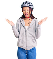 Young beautiful chinese girl wearing bike helmet celebrating victory with happy smile and winner expression with raised hands