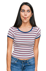 Fototapeta premium Young hispanic girl wearing casual striped t shirt making fish face with lips, crazy and comical gesture. funny expression.