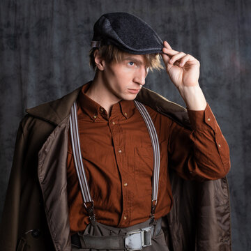 A young guy in military-style clothes, a brown outfit and a flat cap on his head. Posing in the studio on a gray background, close-up