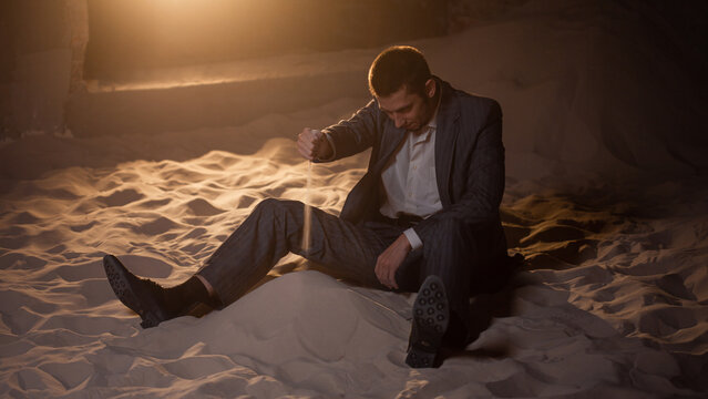 Sandbox for young businesses, startups and financial projects, concept. A young man in a business suit is playing with sand, making impossible plans