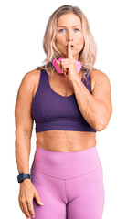 Middle age fit blonde woman wearing gym clothes and using headphones asking to be quiet with finger...