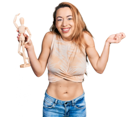 Young caucasian woman holding small wooden manikin screaming proud, celebrating victory and success very excited with raised arm