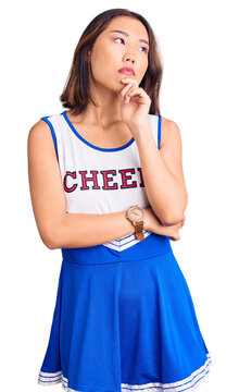 Young beautiful chinese girl wearing cheerleader uniform with hand on chin thinking about question, pensive expression. smiling with thoughtful face. doubt concept.