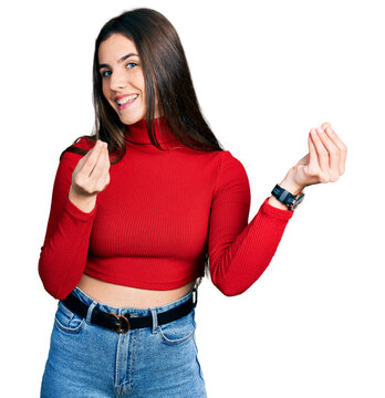 Young brunette teenager wearing red turtleneck sweater doing money gesture with hands, asking for salary payment, millionaire business
