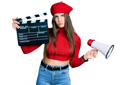 Young brunette teenager holding video film clapboard and megaphone depressed and worry for distress, crying angry and afraid. sad expression.