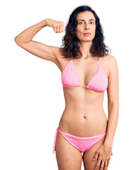 Fototapeta premium Young beautiful hispanic woman wearing bikini strong person showing arm muscle, confident and proud of power
