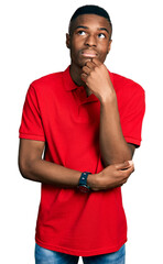 Young african american man wearing casual red t shirt with hand on chin thinking about question,...