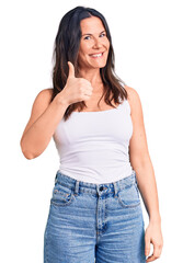 Young beautiful brunette woman wearing casual sleeveless t-shirt doing happy thumbs up gesture with hand. approving expression looking at the camera showing success.