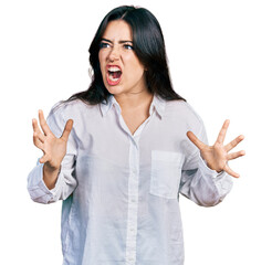 Beautiful hispanic woman wearing casual white shirt crazy and mad shouting and yelling with aggressive expression and arms raised. frustration concept.