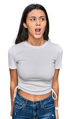 Obraz premium Young hispanic girl wearing casual white t shirt angry and mad screaming frustrated and furious, shouting with anger. rage and aggressive concept.