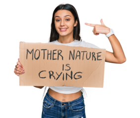 Young hispanic girl holding mother nature is crying protest cardboard banner pointing finger to one self smiling happy and proud