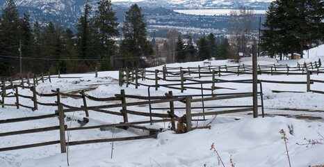 Country home fence line along a twisting driveway covered in snow, and looking out over mountains and a lake.