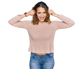 Beautiful young caucasian woman wearing casual sweater smiling pulling ears with fingers, funny...