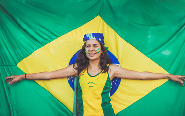 brazilian girl with open arms smiling with brazilian  flag extended behind her