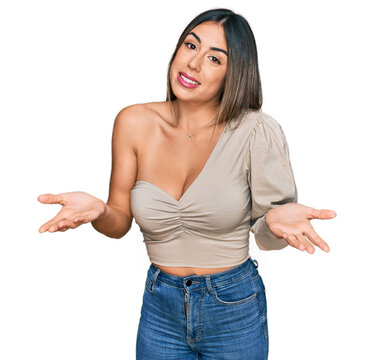 Young hispanic woman wearing casual clothes clueless and confused expression with arms and hands raised. doubt concept.