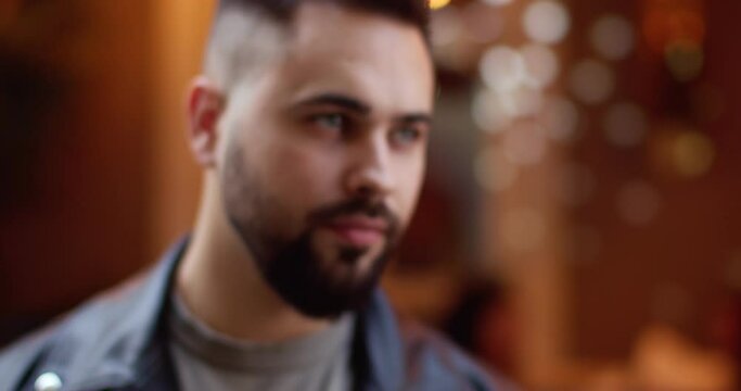 Blurred close up of smiling young male face with beard. Portrait of happy handsome man at decorated street. Outside. Christmas town concept. Holiday decorations. Blurred and focused.