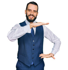 Young man with beard wearing business vest gesturing with hands showing big and large size sign, measure symbol. smiling looking at the camera. measuring concept.