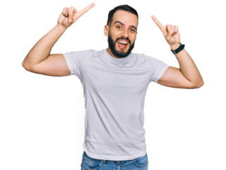 Young man with beard wearing casual white t shirt smiling amazed and surprised and pointing up with fingers and raised arms.