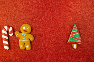 Gingerbread man, candy and Christmas tree on a red background. Gingerbread cookies decorated with icing on a red glitter background. Christmas glitter background. High quality photo