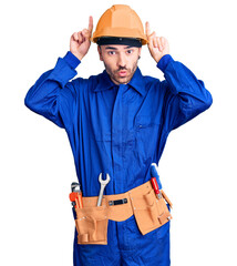 Young hispanic man wearing worker uniform doing funny gesture with finger over head as bull horns