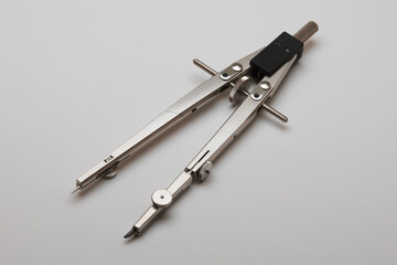 Pair of drawing compasses lying on a plain light background