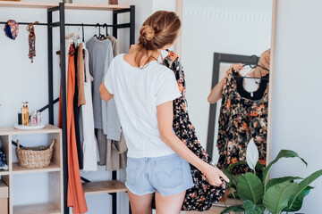woman choosing clothes on clothes rack dressing looking herself in mirror. 