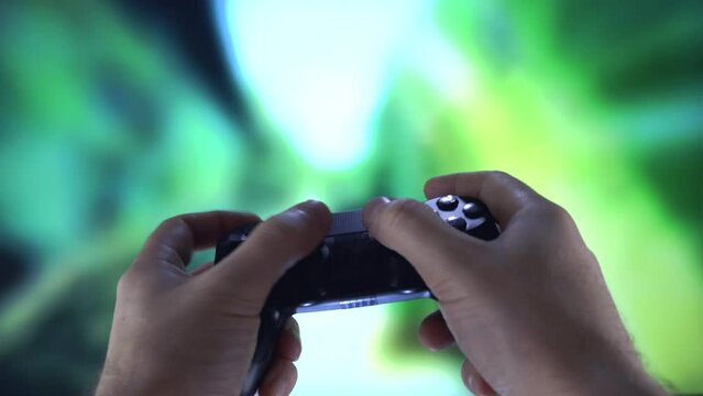 Young man playing an unrecognizable computer video game with joypad on a large blurry screen. Close-up of hands using controller playing video games. Online video game technology and game gambling