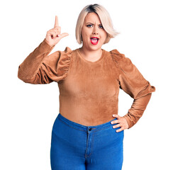 Young blonde plus size woman wearing casual sweater pointing finger up with successful idea. exited...