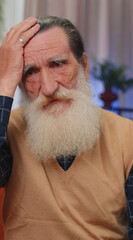 Close-up of sad sick senior old grandfather man at home looks pensive thinks over life concerns or...