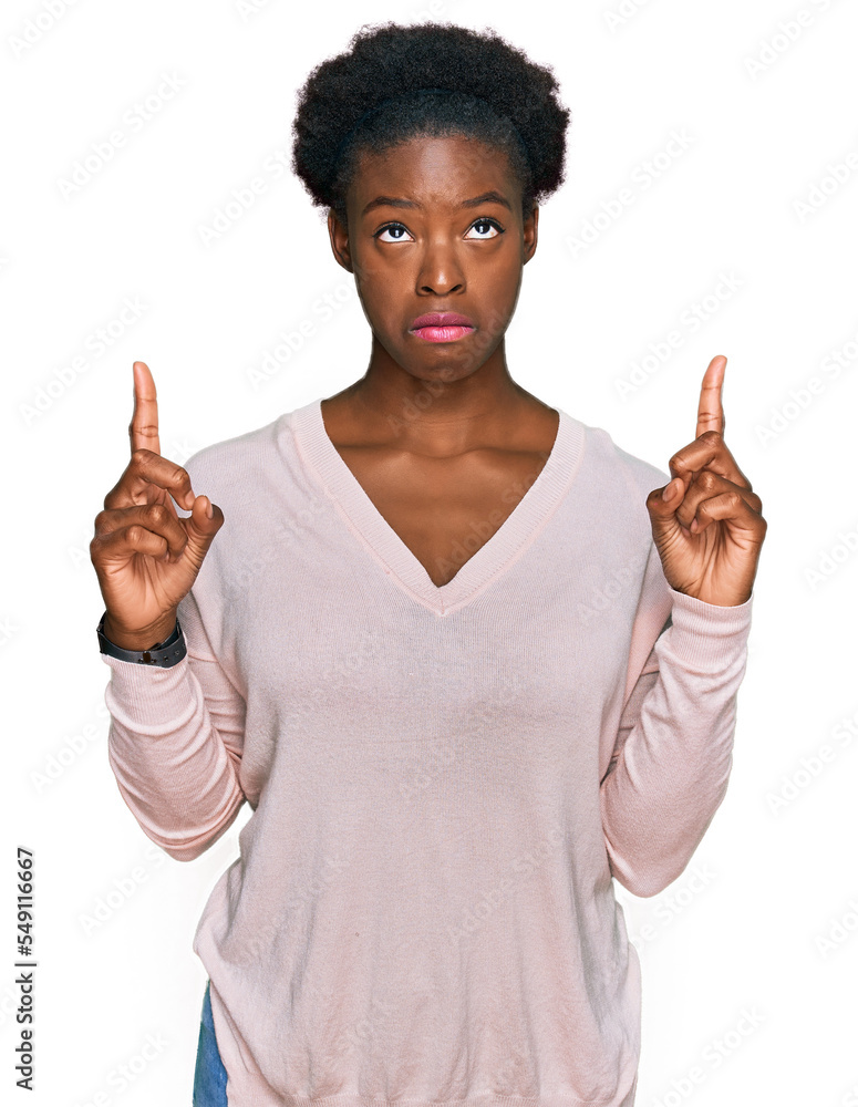 Poster Young african american girl wearing casual clothes pointing up looking sad and upset, indicating direction with fingers, unhappy and depressed.