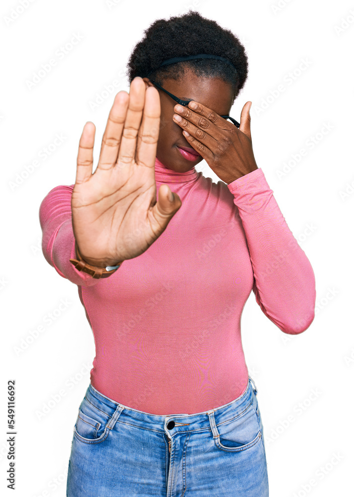 Poster Young african american girl wearing casual clothes and glasses covering eyes with hands and doing stop gesture with sad and fear expression. embarrassed and negative concept.