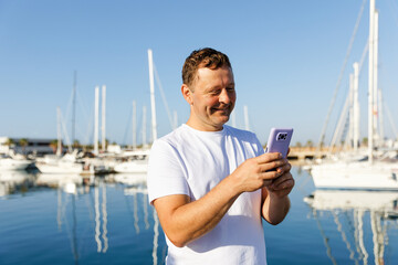 Fototapeta na wymiar A man communicates on the phone against the background of yachts and a marina