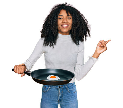 Young african american girl holding skillet with fried egg smiling happy pointing with hand and finger to the side