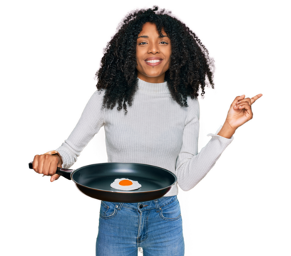 Young african american girl holding skillet with fried egg smiling happy pointing with hand and finger to the side