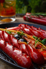 frying pan with sausages, black olives, rosemary. Outdoor with a beverage.