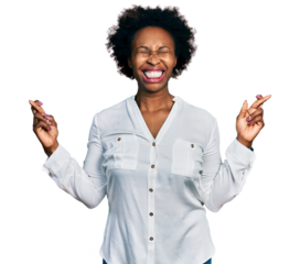 African american woman with afro hair wearing casual white t shirt gesturing finger crossed smiling with hope and eyes closed. luck and superstitious concept.