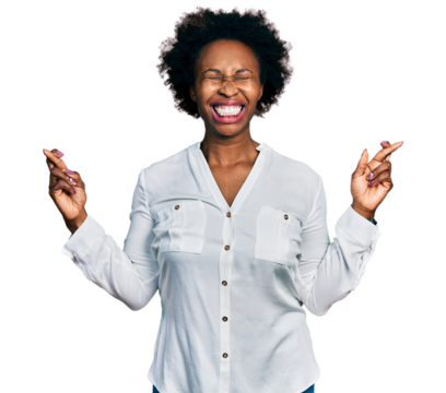 African american woman with afro hair wearing casual white t shirt gesturing finger crossed smiling with hope and eyes closed. luck and superstitious concept.