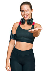 Beautiful blonde woman wearing gym clothes and using headphones smiling friendly offering handshake as greeting and welcoming. successful business.