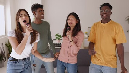 International group of young friends dancing having fun playing karaoke at home party. Multiethnic millennial students enjoying day off at weekend - Friendship and entertainment concept