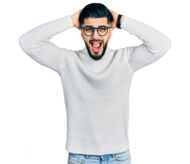 Young arab man with beard wearing elegant turtleneck sweater and glasses crazy and scared with hands on head, afraid and surprised of shock with open mouth