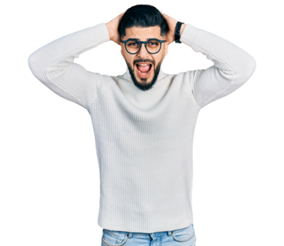 Young arab man with beard wearing elegant turtleneck sweater and glasses crazy and scared with hands on head, afraid and surprised of shock with open mouth