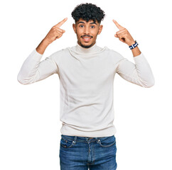Young arab man wearing casual winter sweater smiling pointing to head with both hands finger, great...
