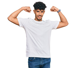 Young arab man wearing casual white t shirt showing arms muscles smiling proud. fitness concept.