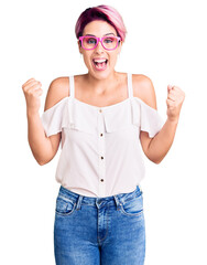 Obraz na płótnie Canvas Young beautiful woman with pink hair wearing casual clothes and glasses celebrating surprised and amazed for success with arms raised and open eyes. winner concept.