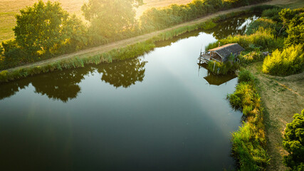 Aerial view of small lake and cabing with a tiny fishing cabin in sunset or sunrise.
