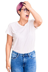 Obraz premium Young beautiful woman with pink hair wearing casual clothes and glasses surprised with hand on head for mistake, remember error. forgot, bad memory concept.